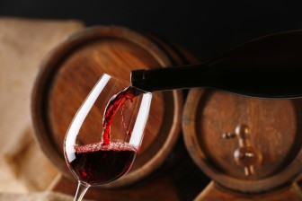 Pouring red wine from bottle into glass with wooden wine casks o