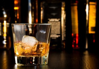 Whiskey Glass With Ice In Front Of Bottles