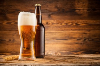 Glass and bottle of beer with wheat ears on wooden planks